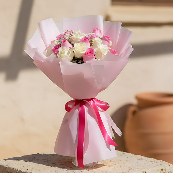 Hand-tied bouquet of pink and white roses with gypsophila wrapped in soft light pink paper