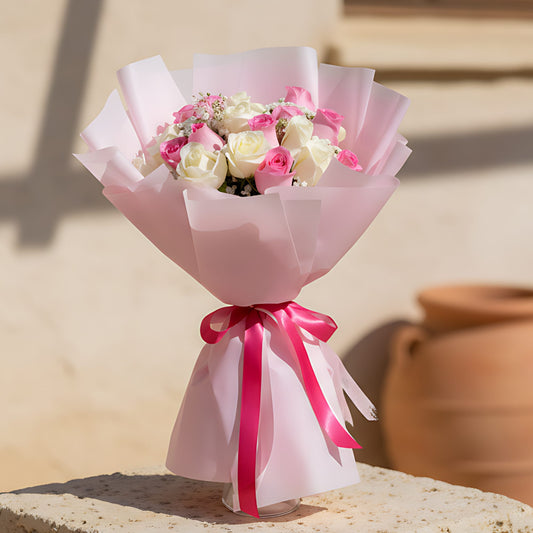 Hand-tied bouquet of pink and white roses with gypsophila wrapped in soft light pink paper