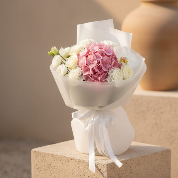 Pink hydrangea bouquet with white roses and orchid wrapped in elegant white paper with ribbon.
