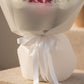 Close-up detail of white bouquet wrapping and ribbon beneath pink hydrangea flowers.