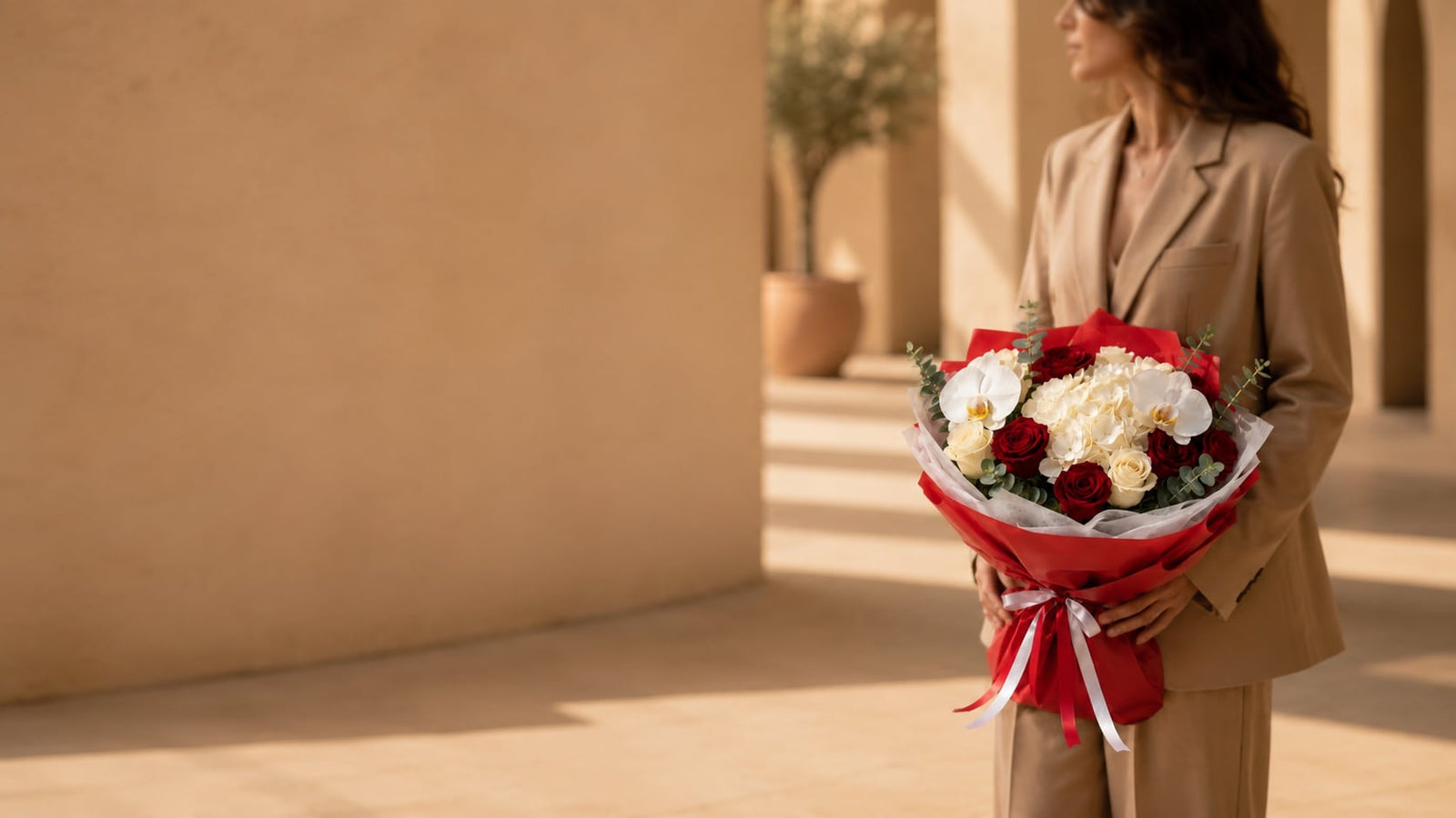 Woman in a beige suit holding a red and white rose bouquet with orchid accents — New Arrivals by Aiwa Flowers Dubai