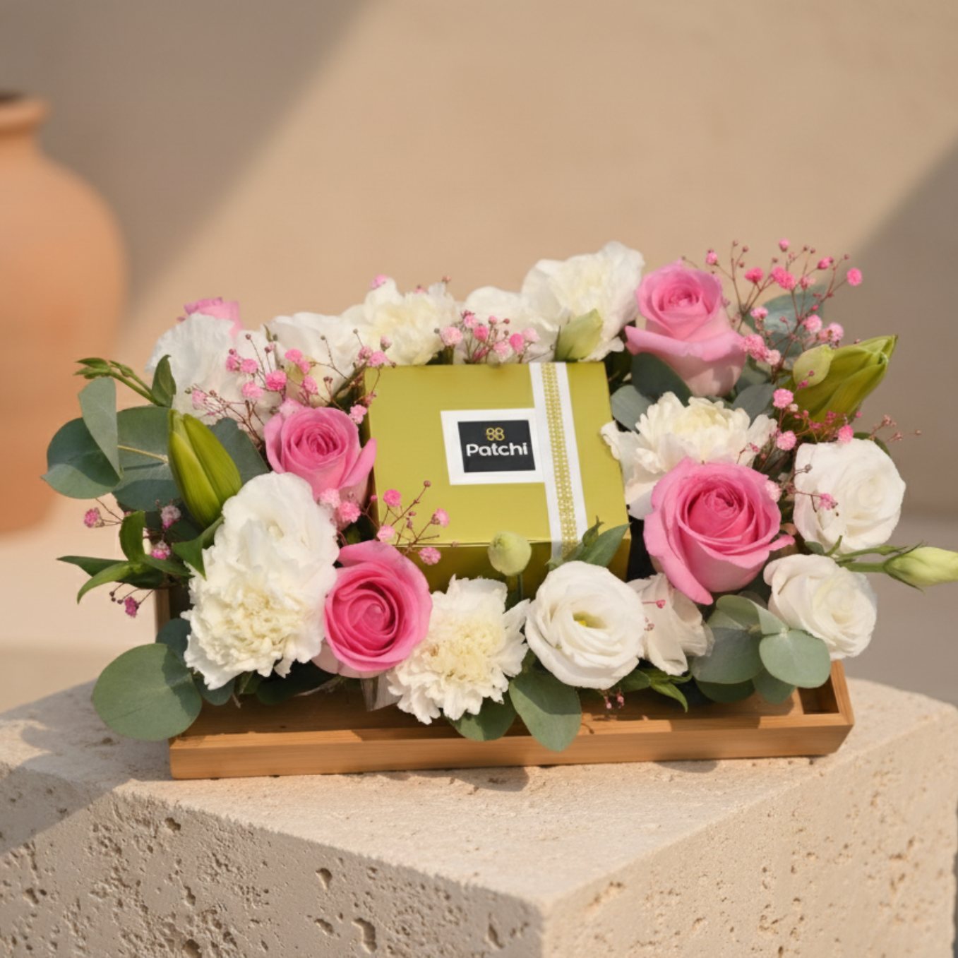 Patchi chocolate platter with pink roses, white carnations, lisianthus and lilies arranged on a wooden tray.