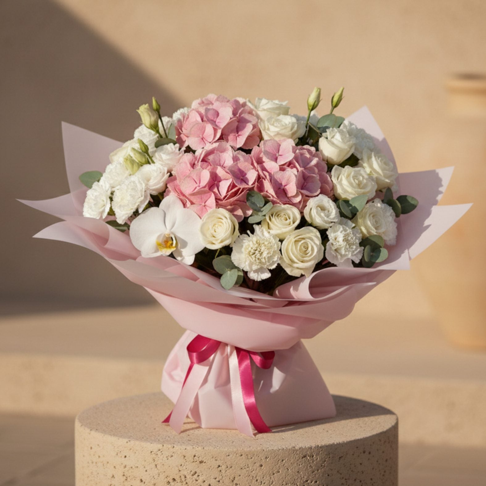Pink hydrangea bouquet with white roses, orchid, and eucalyptus wrapped in blush pink paper.