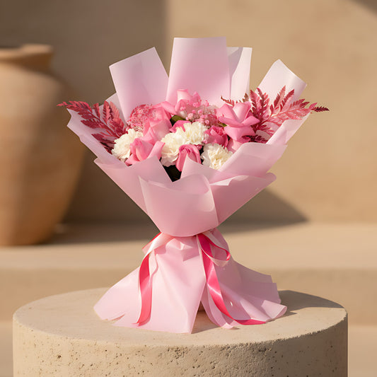 Hand-tied bouquet of pink roses with white carnations, gypsophila, and pink fern wrapped in pink paper