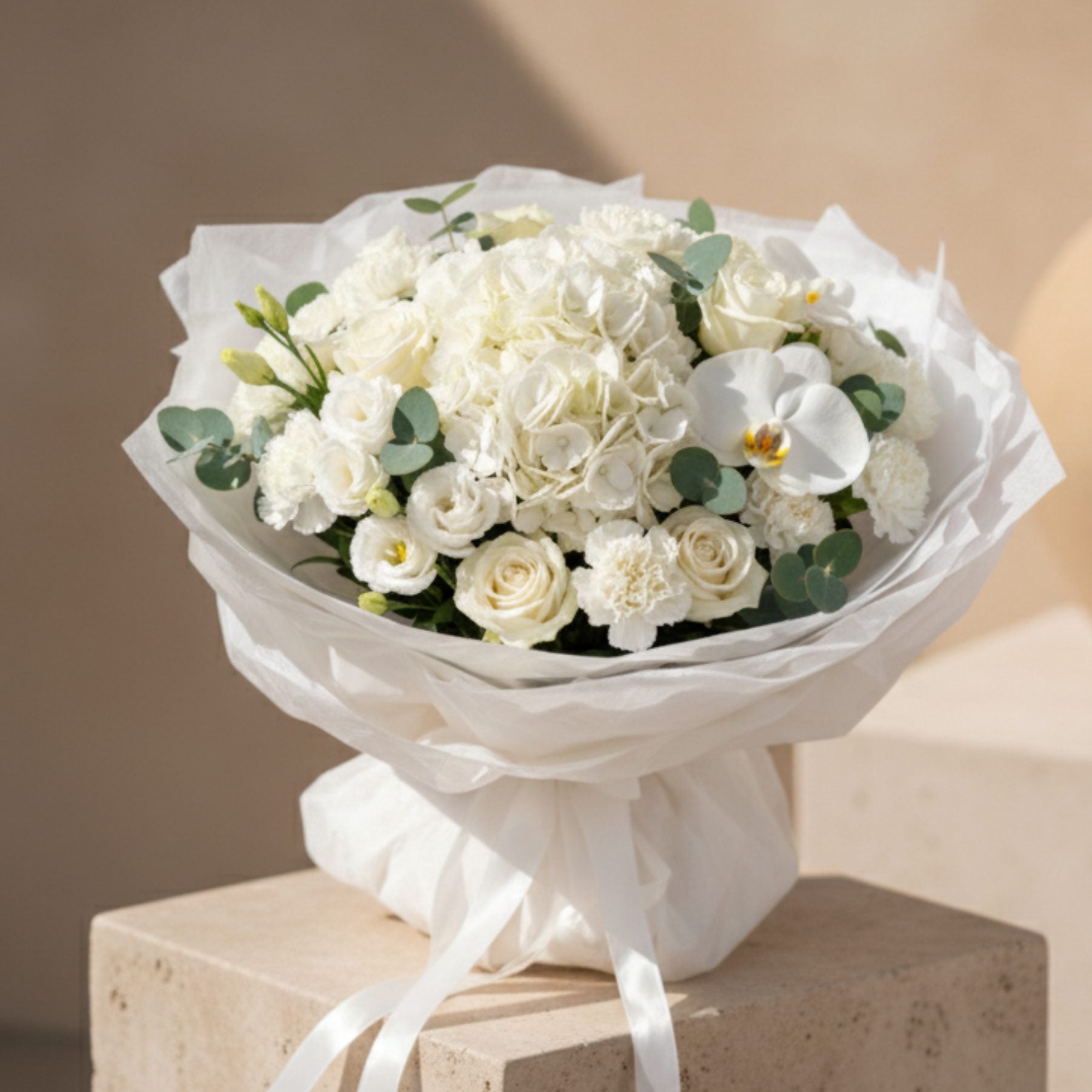 White hydrangea bouquet with roses, orchid, and eucalyptus wrapped in elegant white paper.