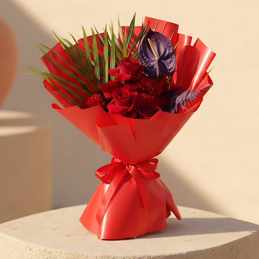 Hand-tied bouquet with red roses, carnations, anthurium, and greenery wrapped in elegant red paper