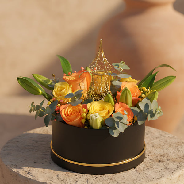 Luxury Ramadan flower box with yellow and orange roses, white lilies, gypsophila, eucalyptus, and a gold coffee pot accent arranged in a black round box, available in Dubai.