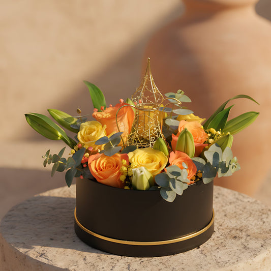 Luxury Ramadan flower box with yellow and orange roses, white lilies, gypsophila, eucalyptus, and a gold coffee pot accent arranged in a black round box, available in Dubai.