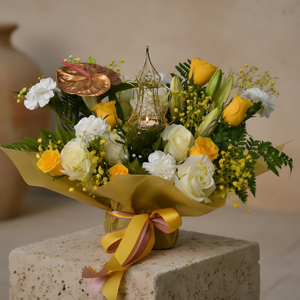 Luxury Ramadan bouquet with yellow and white roses, white carnations, a lily stem, gold anthurium, gypsophila, and a gold candle lantern, wrapped in elegant gold packaging, available for delivery in Dubai.