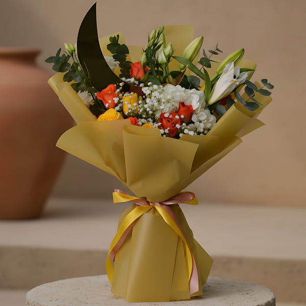Luxury Ramadan hand-tied bouquet with yellow and orange roses, lisianthus, lily stems, white hydrangea, eucalyptus, gypsophila, and a moon-shaped topper in gold wrapping, available for delivery in Dubai.