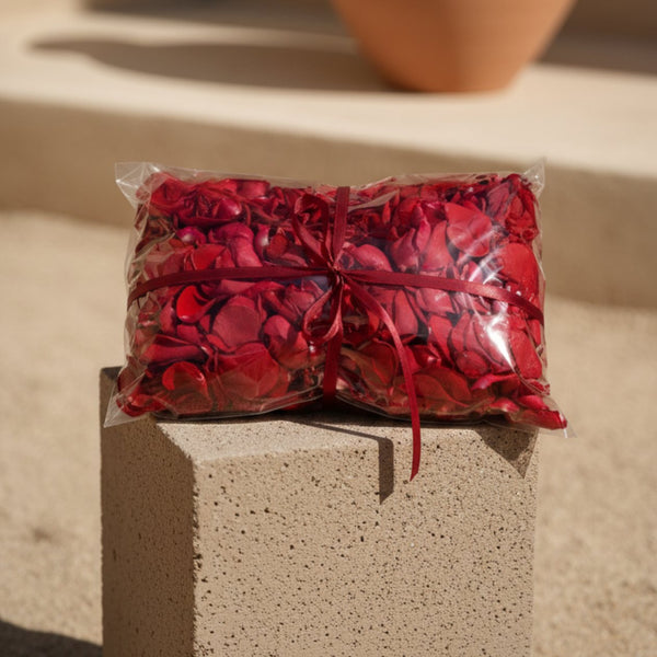 Bag of red rose petals wrapped in transparent packaging with red ribbon on a beige pedestal
