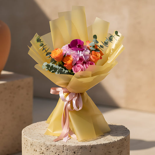 Hand-tied bouquet with pink hydrangea, purple orchid, pink and orange roses, and eucalyptus wrapped in gold paper