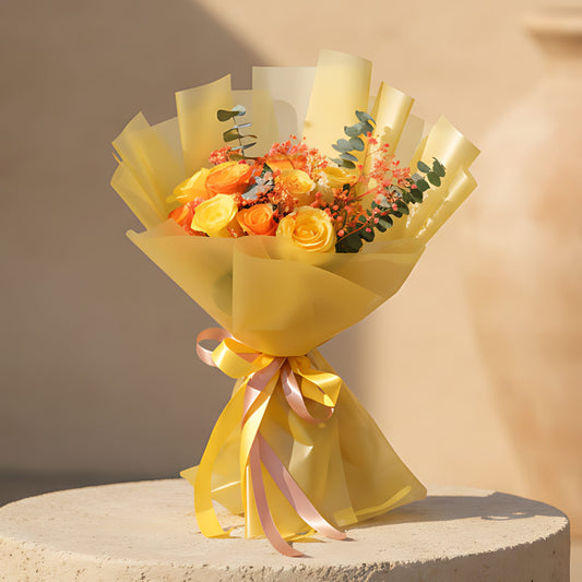Hand-tied bouquet of yellow and orange roses with orange gypsophila and eucalyptus wrapped in gold paper
