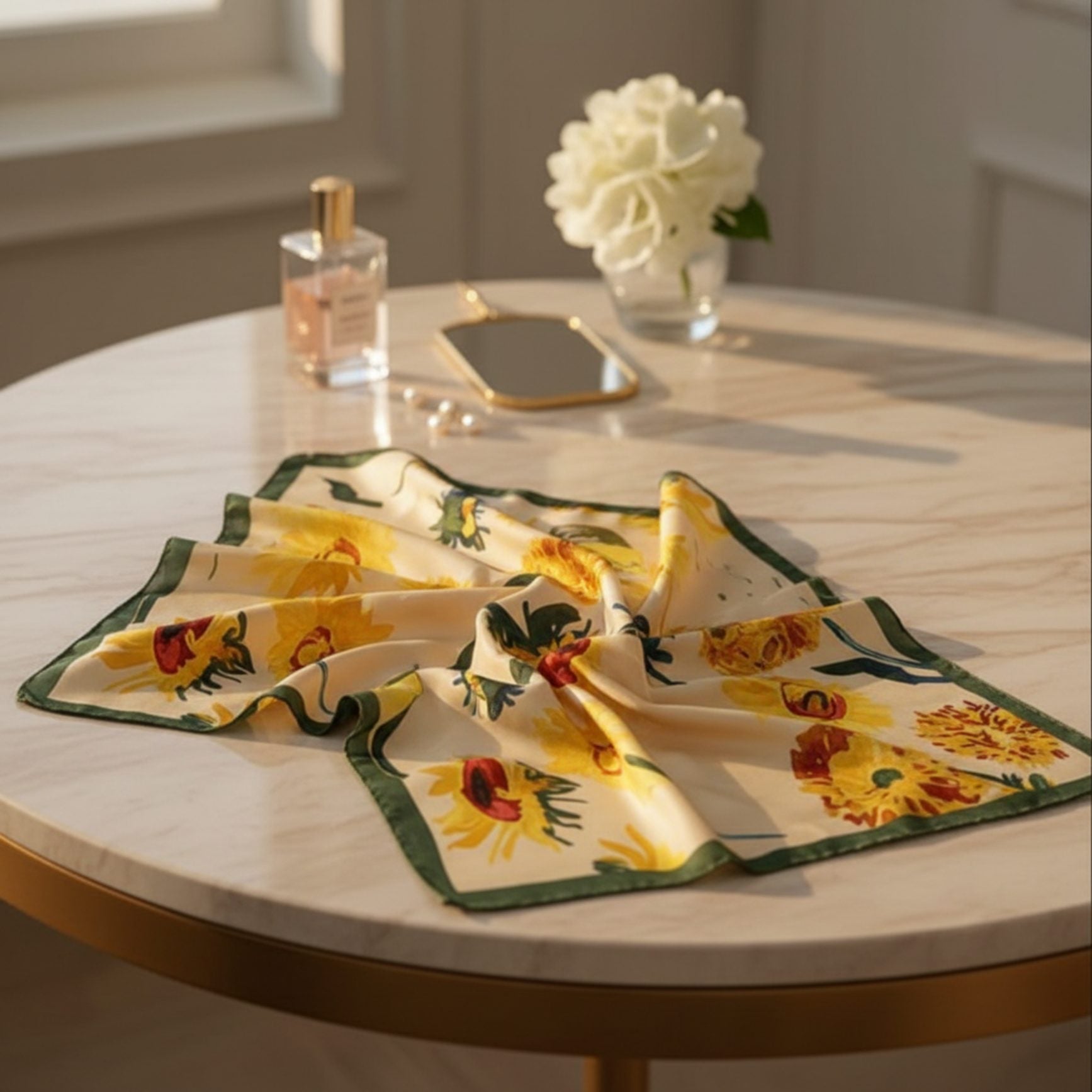 Sunflower print silk scarf displayed on table with perfume, mirror and pearl accessories.