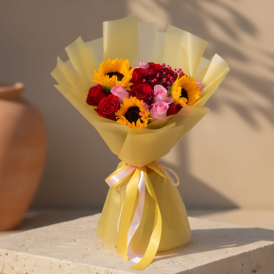 Hand-tied bouquet with sunflowers, red and pink roses, and gypsophila wrapped in gold paper