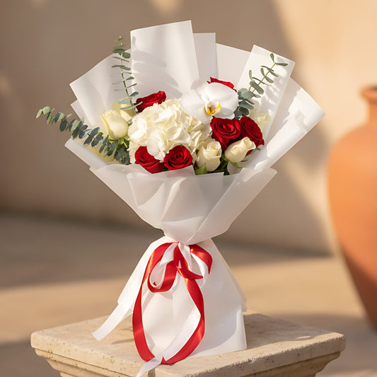Hand-tied bouquet with white hydrangea, white orchid, red and white roses, and eucalyptus wrapped in white paper