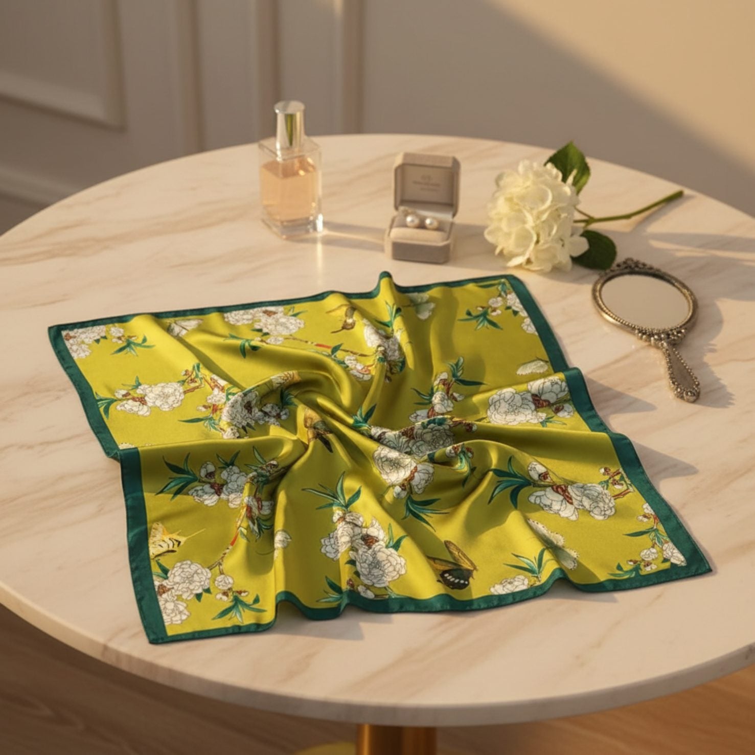 Floral printed silk scarf displayed on table with perfume and jewelry.