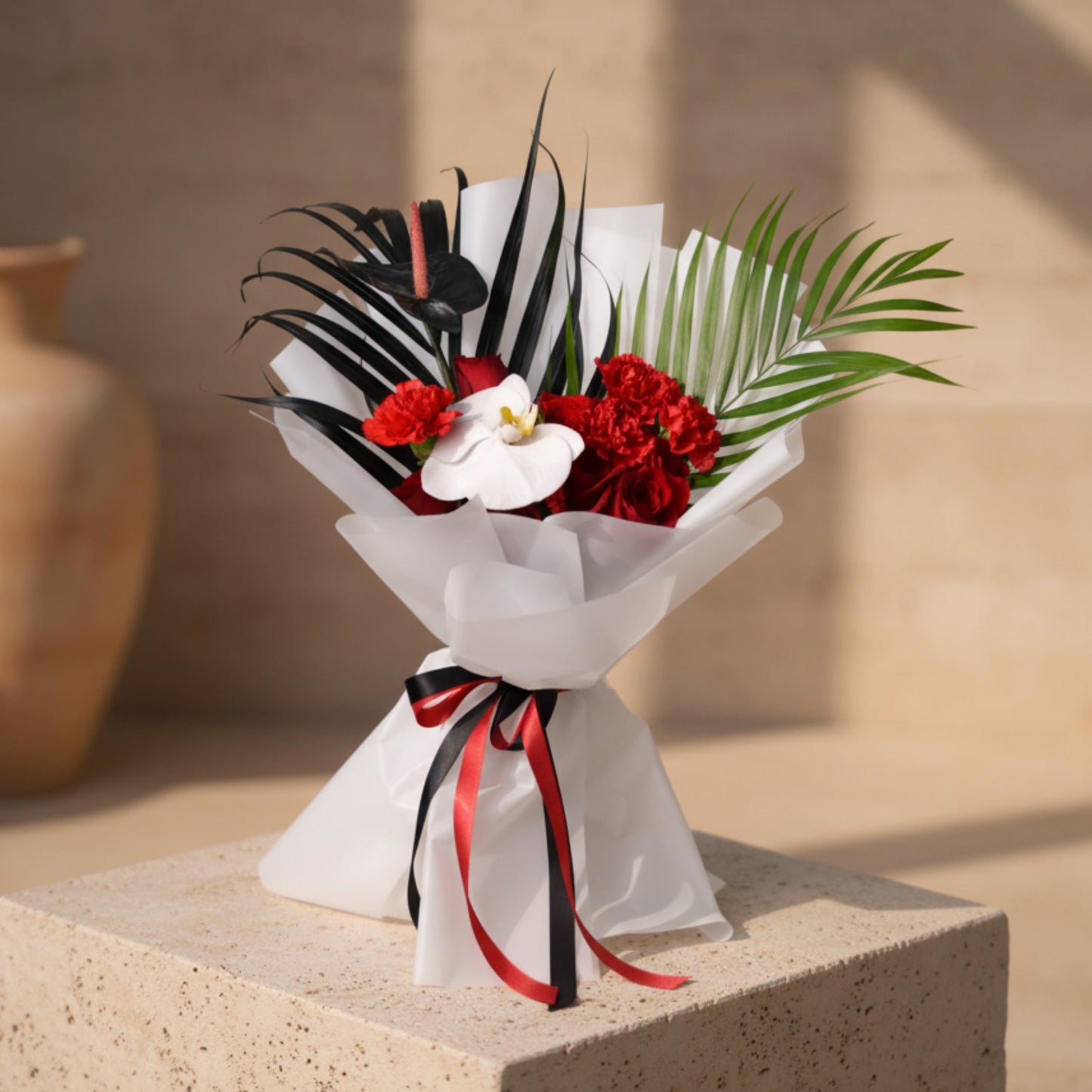 Unity bouquet with red roses, red carnations, white orchid and black anthurium in white wrapping.