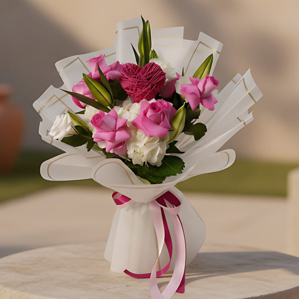 Hand-tied bouquet of pink roses with lisianthus, white hydrangea, lilies, and heart detail in trendy wrapping
