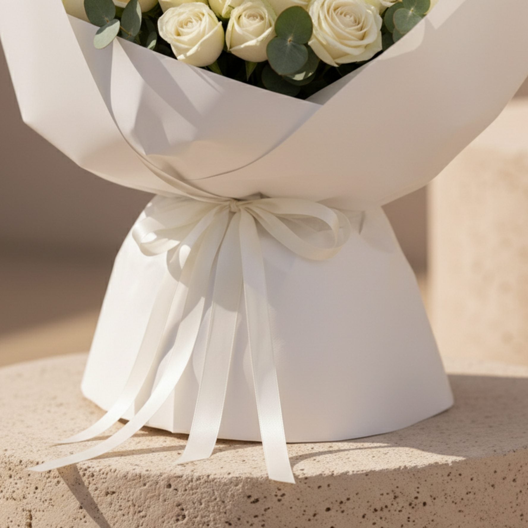 Close-up detail of white bouquet wrapping and ribbon on White Poise rose arrangement.