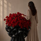 Woman beside a large red rose bouquet in black branded wrapping - Amour Charm by AIWA Flowers
