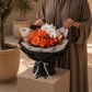 Woman holding a bold orange rose and white orchid bouquet by AIWA Flowers Dubai