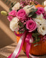 Close-up of pink roses, white carnations and eucalyptus in the Candy Muncher pumpkin arrangement