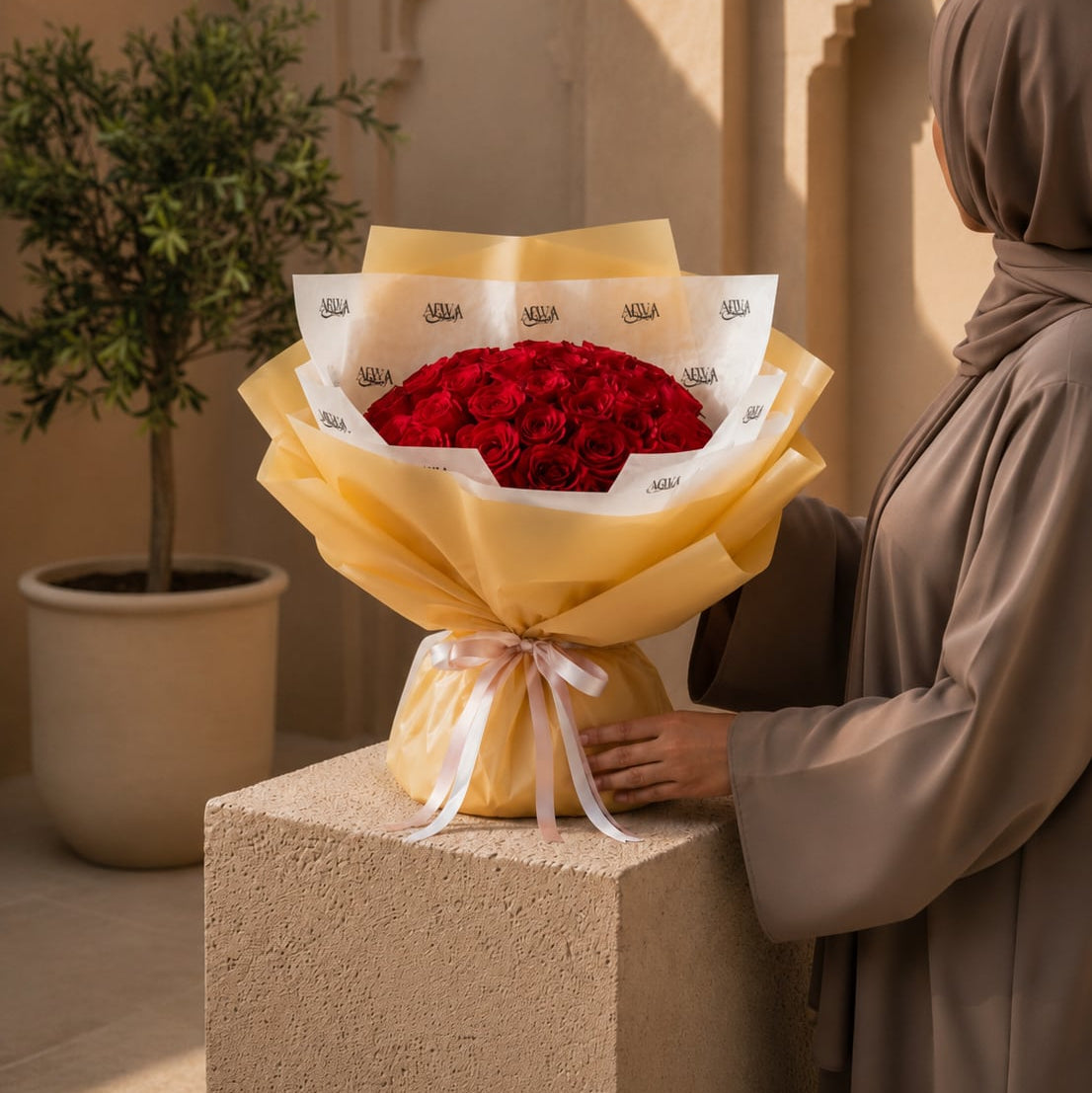 Woman holding a red rose bouquet in gold wrapping by AIWA Flowers Dubai