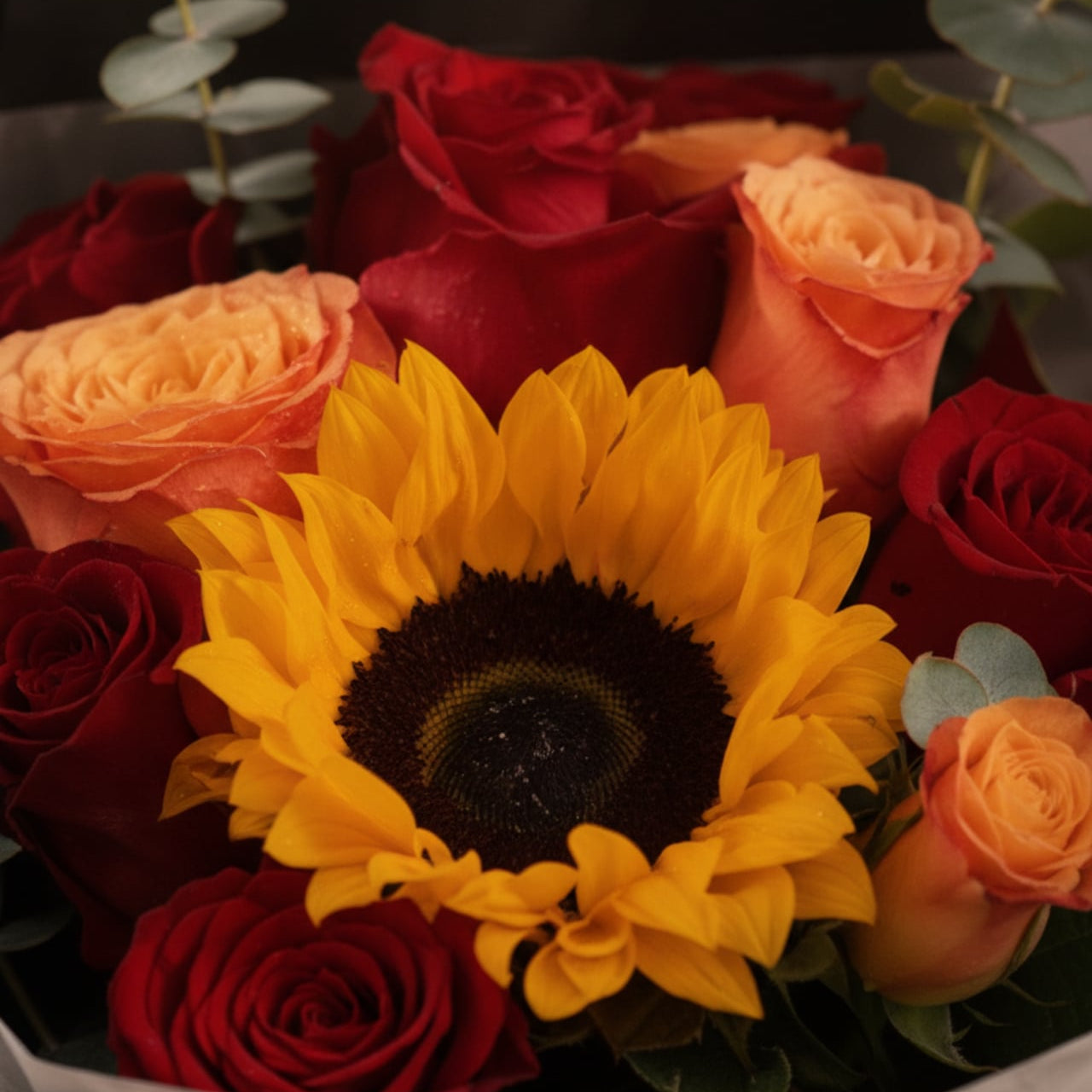 Close-up of sunflower with red and orange roses by AIWA Flowers Dubai