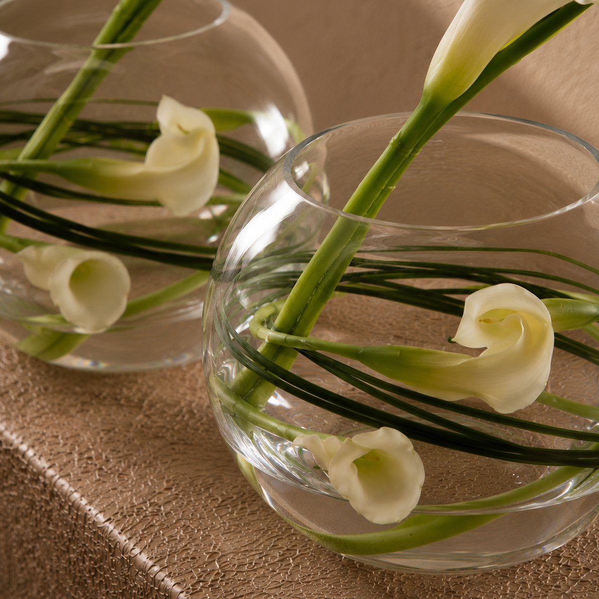 Close-up of white calla lilies with bear grass in a clear glass bubble vase - Laura by AIWA Flowers
