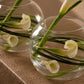 Close-up of white calla lilies with bear grass in a clear glass bubble vase - Laura by AIWA Flowers