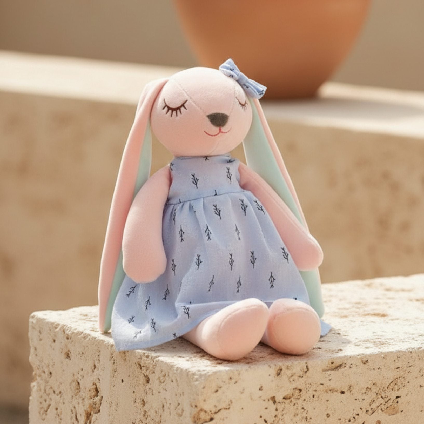 Soft plush bunny toy with pastel pink and blue colors sitting on stone surface, gift by Aiwa Flowers Dubai