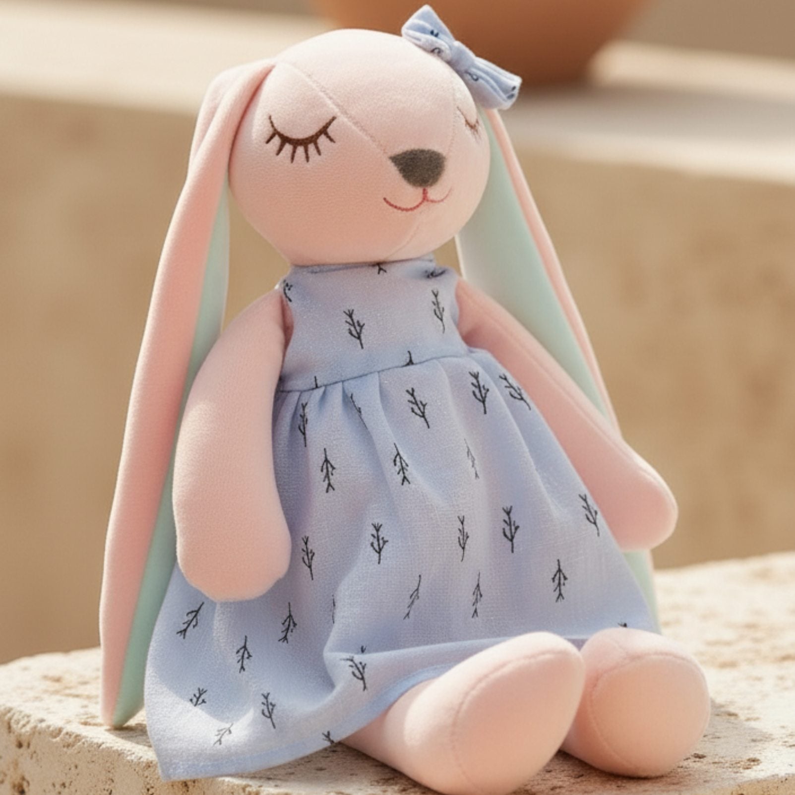 Close-up of pastel bunny plush toy with embroidered face and blue dress, soft gift idea