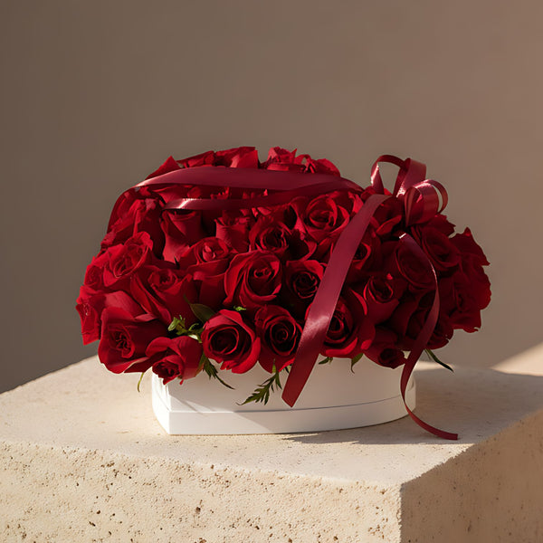 Love Bloom white heart-shaped box with 55 to 65 fresh red roses
