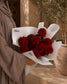 Lover's Gift red rose bouquet wrapped in white AIWA-branded paper, held outdoors by a person in a taupe abaya.