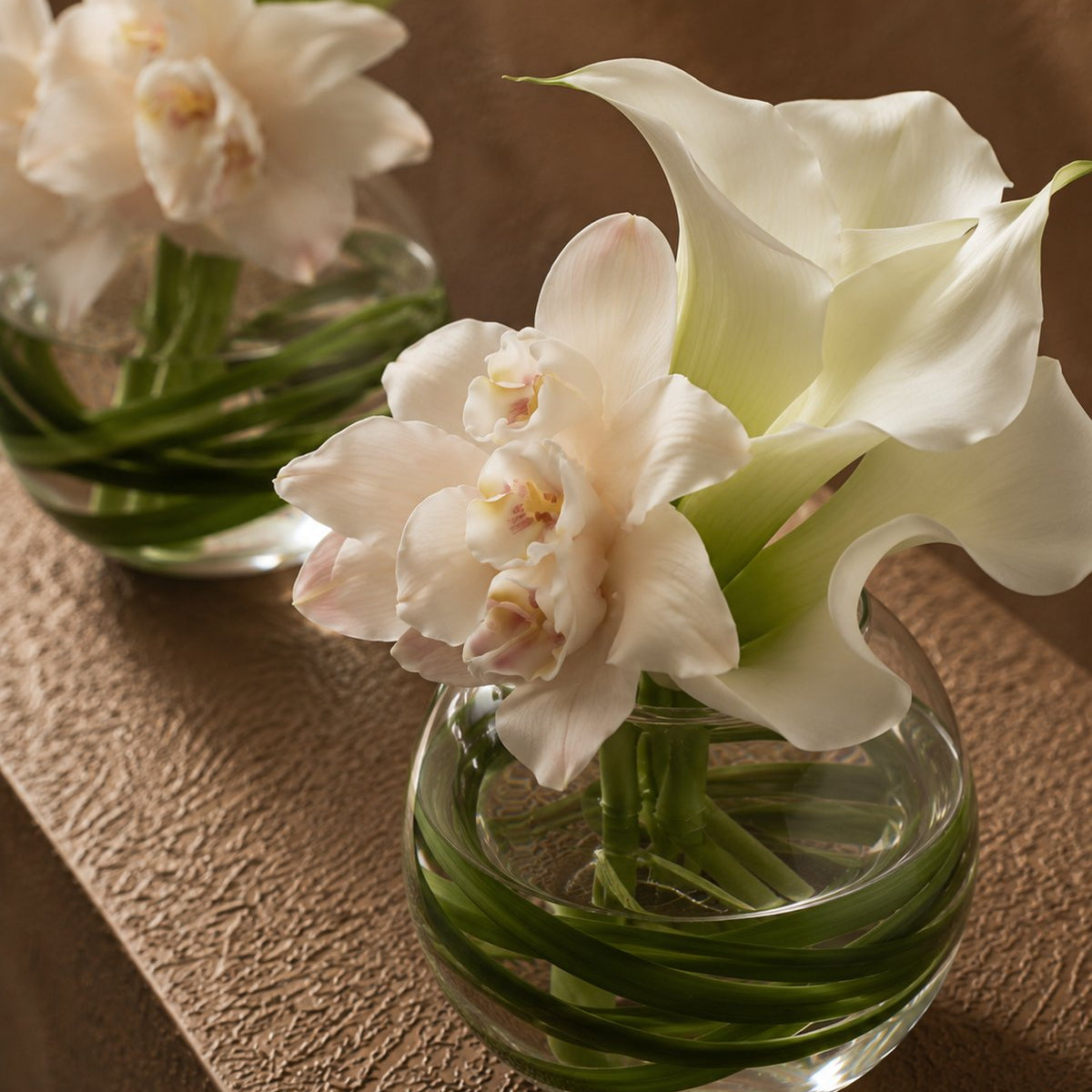 Close-up of Mila blush orchids and white calla lilies with bear grass by AIWA Flowers