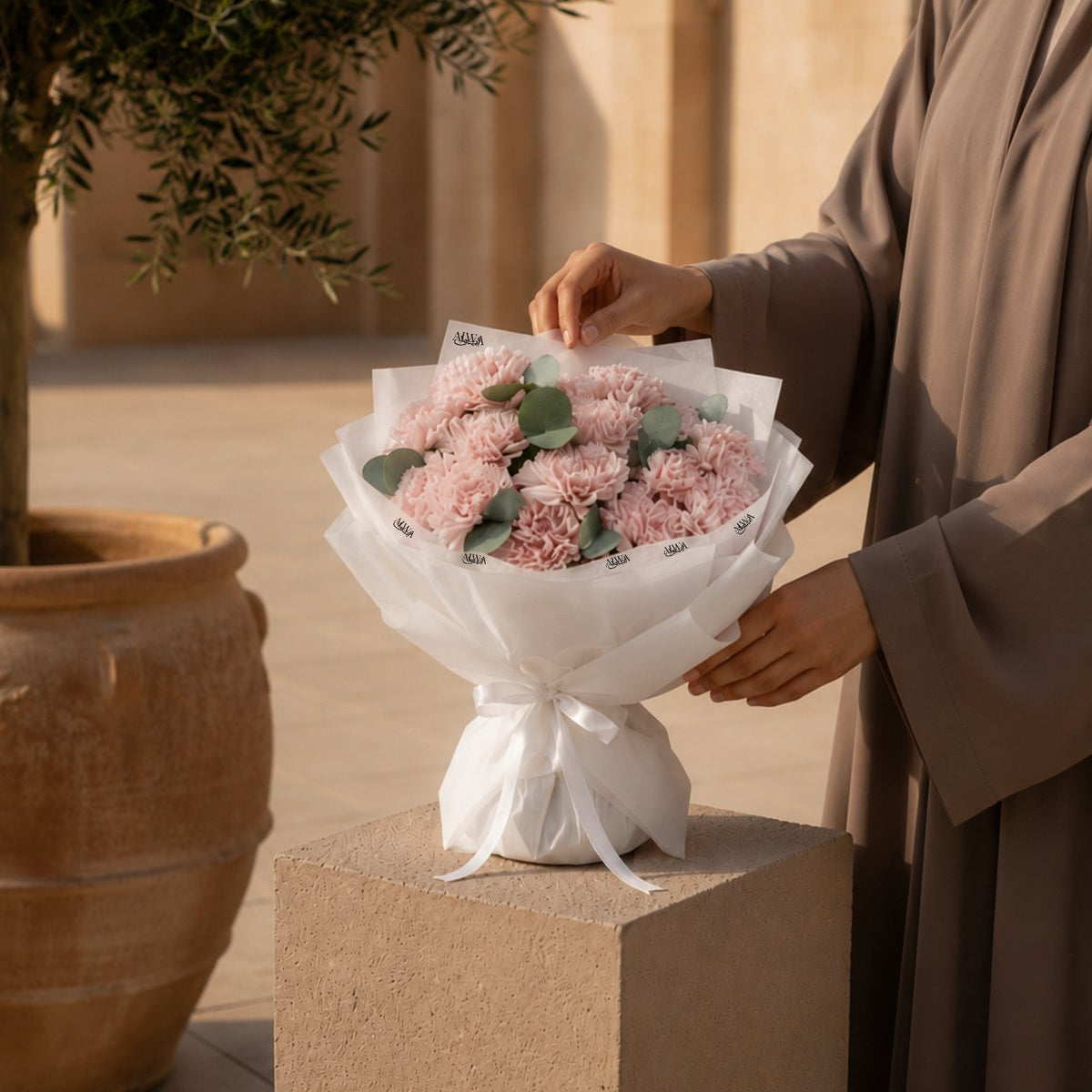 Woman holding a pink carnation bouquet with eucalyptus in white wrap - Moments with Her by AIWA Flowers