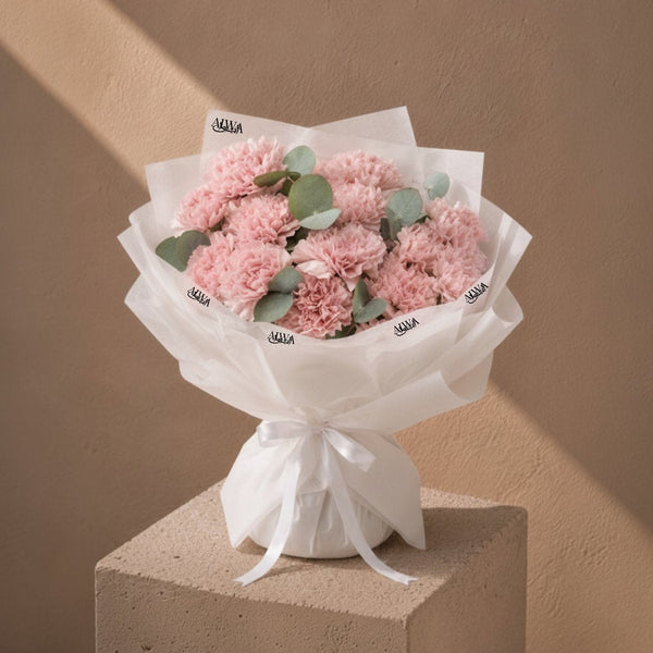 Moments with Her pink carnation bouquet in white wrapping on a plinth by AIWA Flowers
