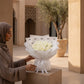 Woman holding a white rose bouquet in a sunlit courtyard - Niveous White by AIWA Flowers