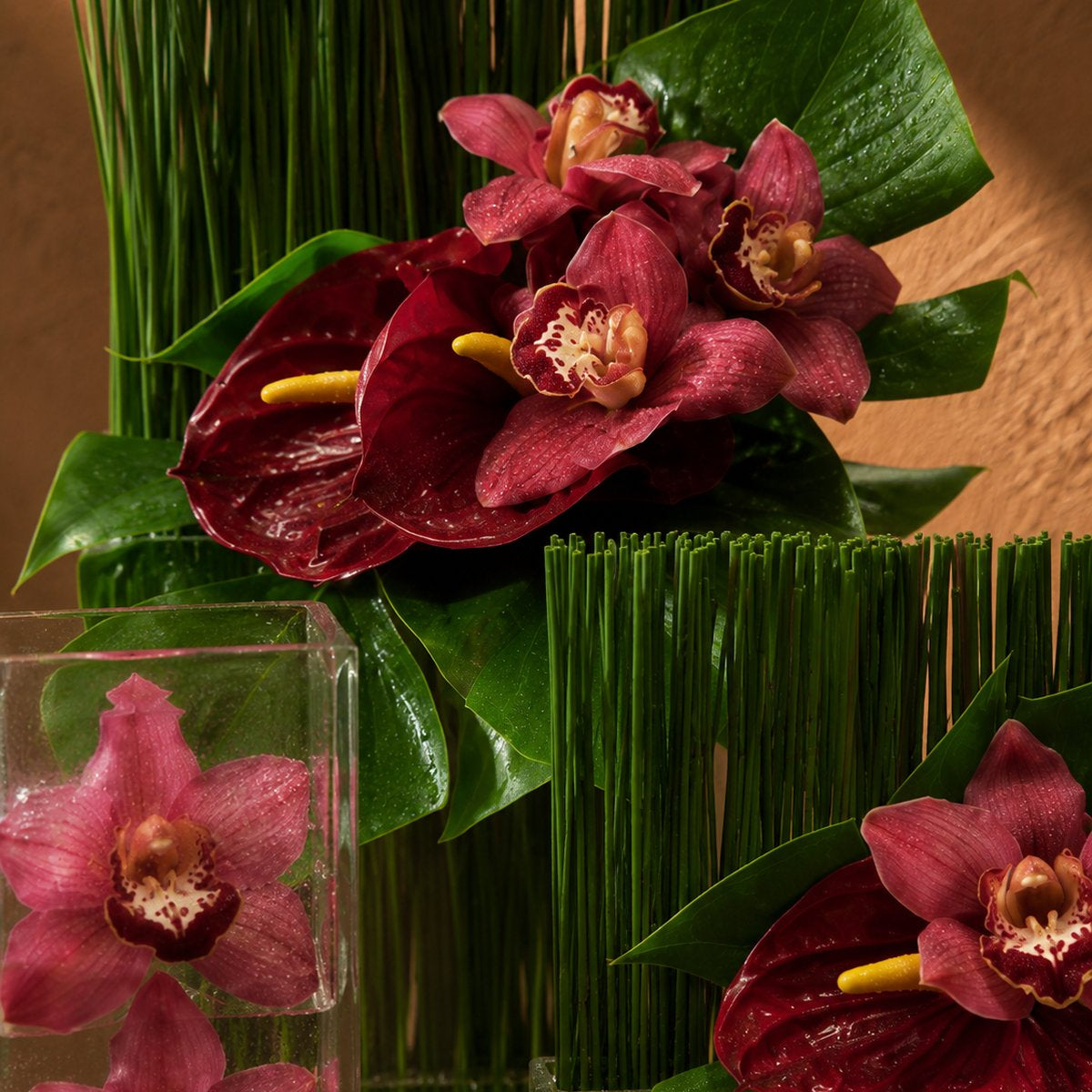 Burgundy cymbidium orchids and red anthurium with tropical greens in clear glass - Nora by AIWA Flowers