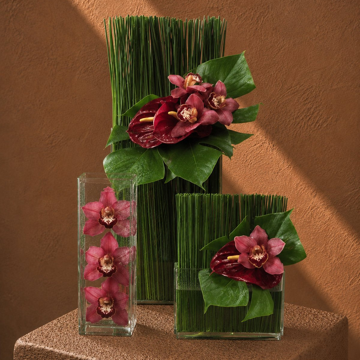 Nora burgundy orchid and red anthurium arrangement with green reeds in tall clear vases by AIWA Flowers