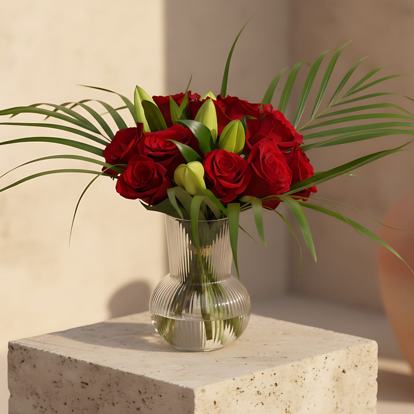 Nora arrangement with red roses, lilies and areca leaves in a clear glass vase
