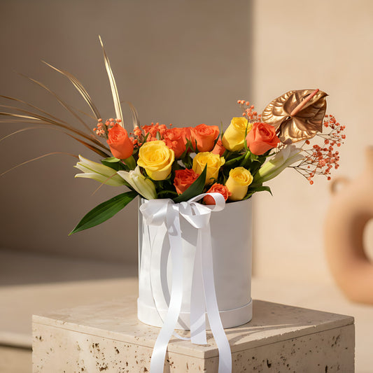 Ochre white velvet round flower box with orange and yellow roses, white lilies and golden anthurium