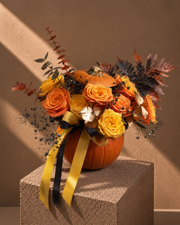 Omen Halloween arrangement of orange and yellow roses in a fresh pumpkin with gold and black ribbons