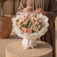 Woman holding a lush blush garden-rose bouquet in white wrap - Palais de Rose by AIWA Flowers