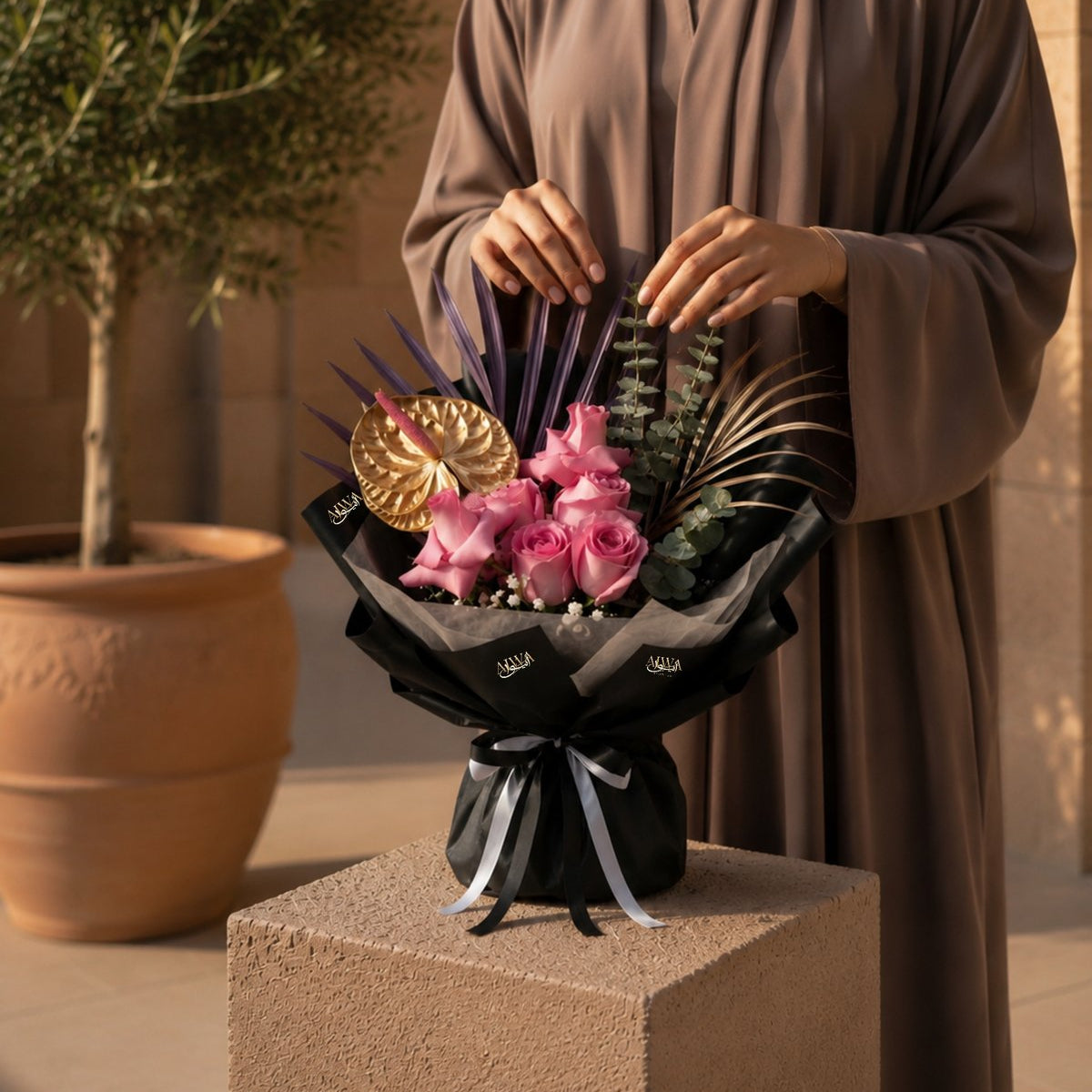 Woman holding a pink rose bouquet with gold anthurium and purple palm in black wrap - Purple Crush by AIWA Flowers