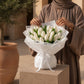Woman holding a bouquet of white tulips in white wrap - Radiant Tulips by AIWA Flowers