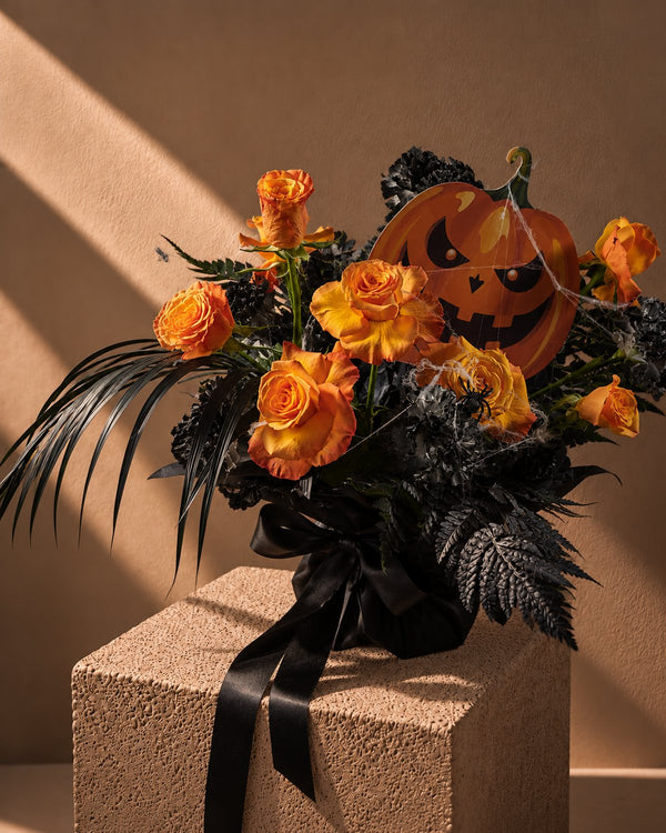 Spooky Spell Halloween bouquet of orange roses and black carnations with a jack-o'-lantern pick