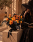 Spooky Spell jack-o'-lantern bouquet styled beside a woman reading in a witch hat
