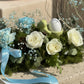 Close-up of white roses, blue carnations, and ceramic bunny egg holder in moss floral arrangement, Easter centerpiece Dubai